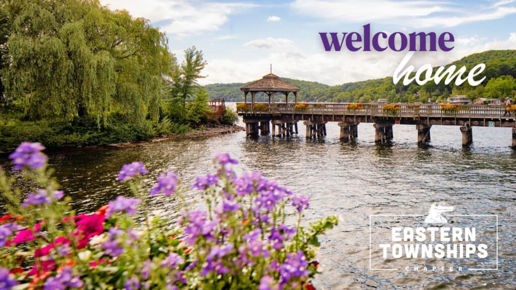 Landscape view of a the pedestrian bridge in North Hatley with the words "welcome home" and "eastern townships chapter"