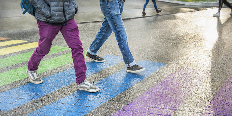 Two students crossing a rainbow painted crosswalk on campus.
