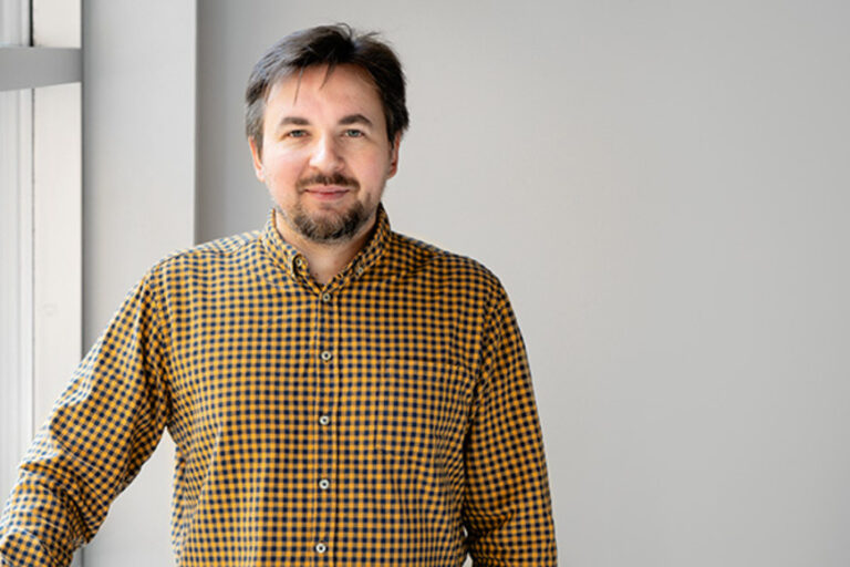 Alex Miltsov in front of a window in a yellow checked shirt.