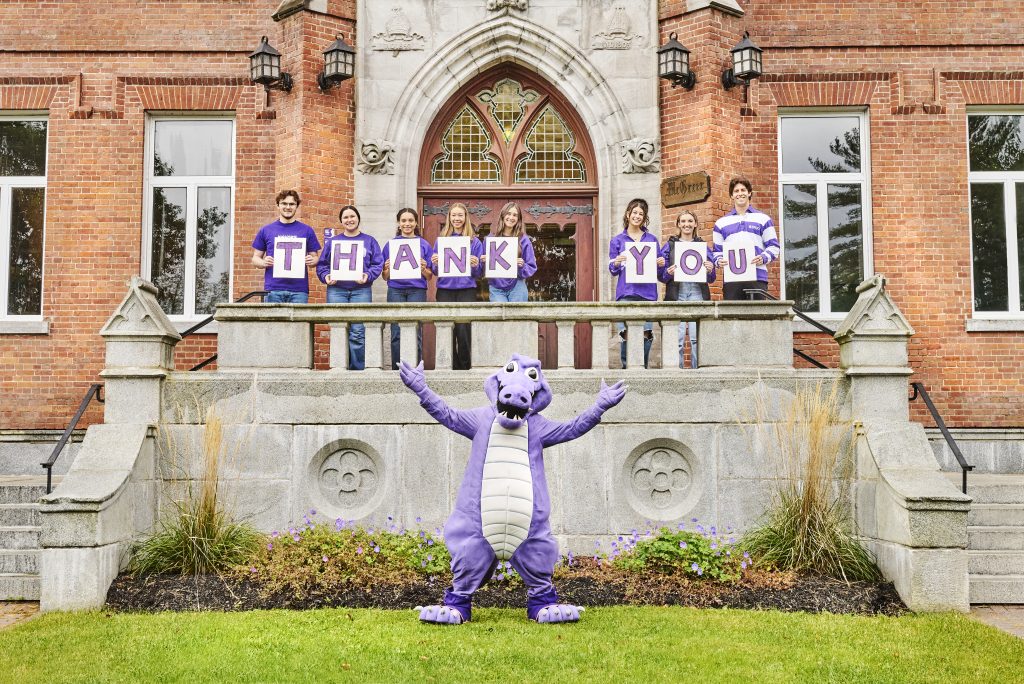 Students holding signs to form the work "Thank you" with the Giater mascot standing below them.