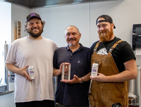 A photo of the three winners of the CBAC prize smiling and holding a can of beer each.