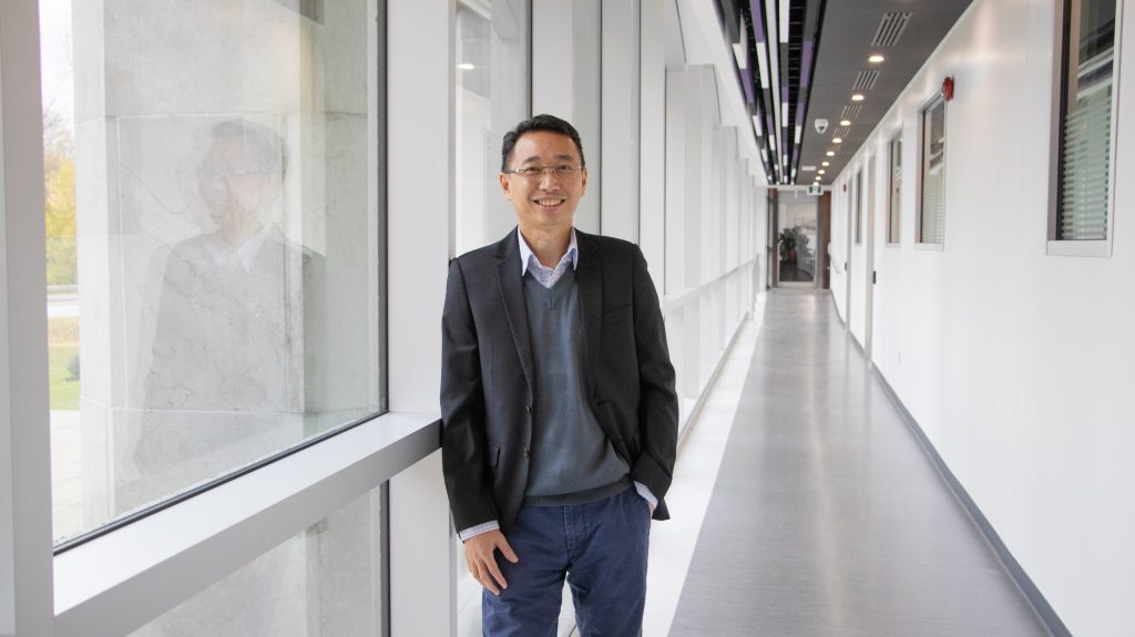 Dr. Augustian Sutrisno smiling at the camera in a long windowed hallway.
