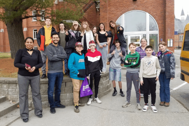 Dr. Sarathi and her 2025 workshop. A group of adults and preteens standing outside the Johnson building on Bishop's campus, near the bus stop.