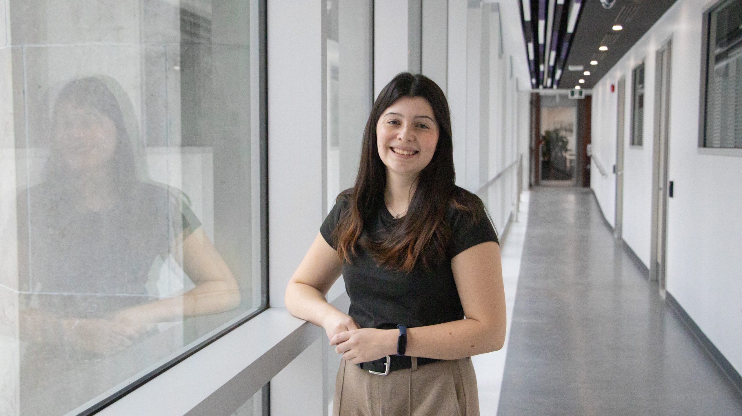 A photo of a young woman with brown hair standing in a windowed hallway. Her name is Elizabeth Garneau.