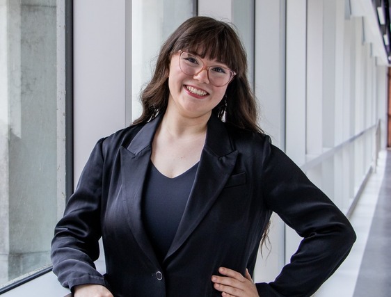 Sonoma Browley smiling in front of windows. She has a suit jacket on, brown hair, and bangs.