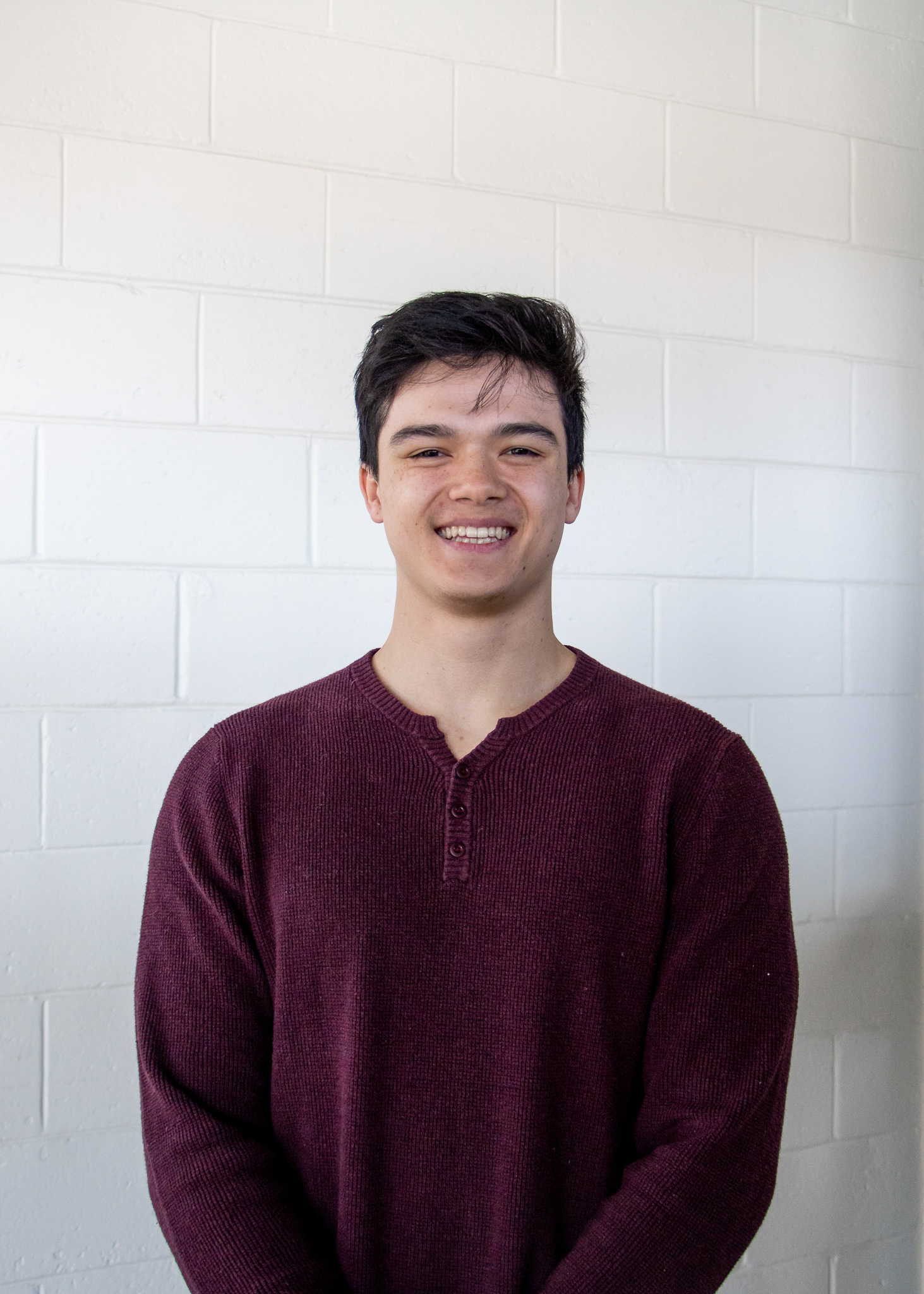 A young man in a red sweater against a white wall. He is Joen Blumer.
