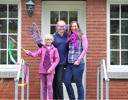 Photo of monthly donor, Kylie, with her family dressed in purple Bishop's gear in front of the alumni house.