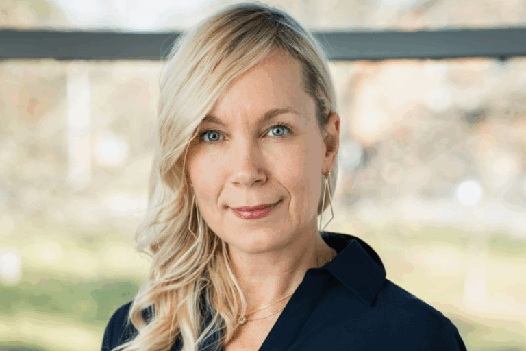 Dr. Joanne Pattison-Meek, a blonde woman in a black shirt, stands in front of a fuzzy nature background.