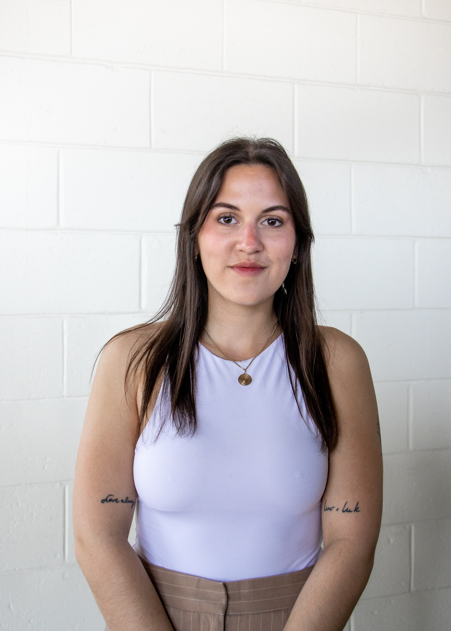 A photo of a young woman with brown hair in front of a white wall. She is Sasha Kardos-Machado.
