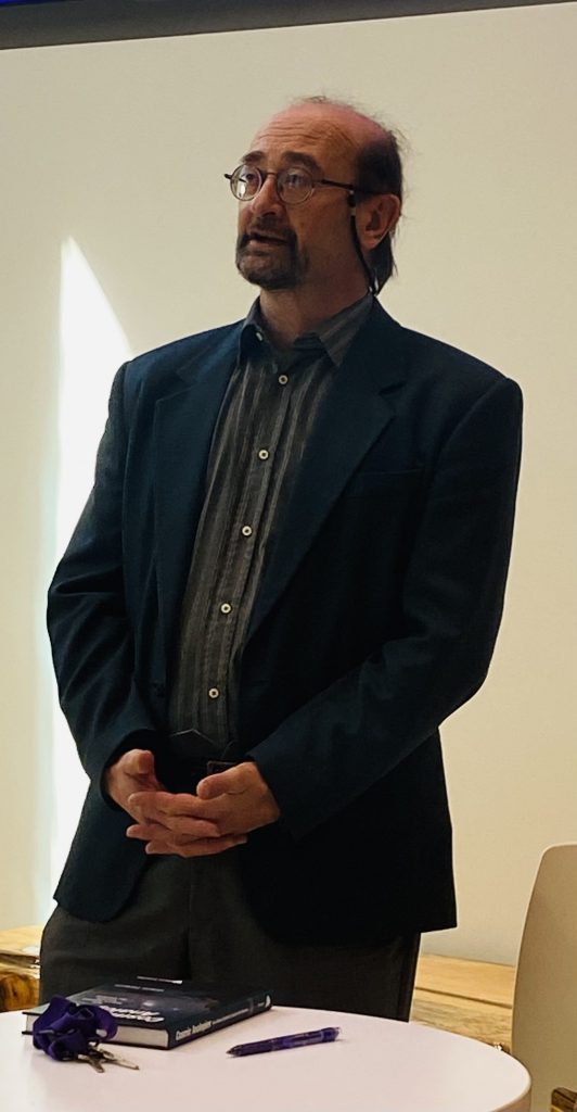Dr. Valerio Faraoni, a man with glasses and a button-up shirt, speaks to a group off-camera.